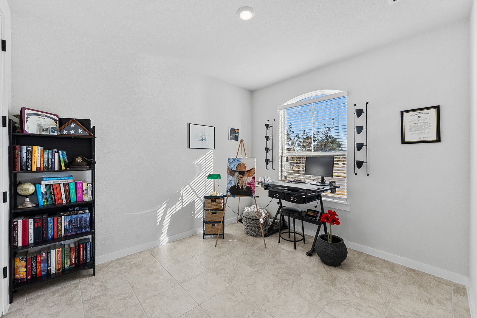 Secondary bedroom used as office/art studio with bookshelf, easel, desk and arched window