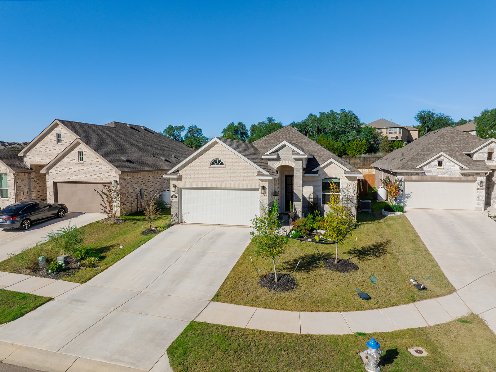 Front exterior from street — single-story brick home with 2-car garage, young trees and manicured lawn